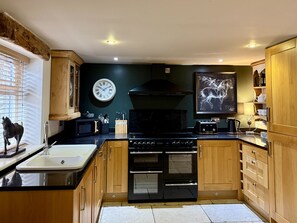 Una cocina con armarios de madera, una estufa negra, un microondas y un reloj en la pared.