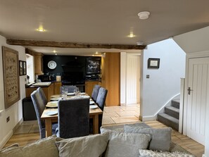 A dining area with a table set for four, a kitchen in the background, and a staircase leading to an upper level.