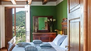 Een slaapkamer met een houten bed, een dressoir en een spiegel. Er is een balkon met uitzicht op groen.
