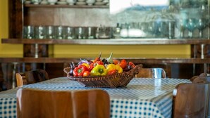 Een eettafel met een geruit tafelkleed en een rieten schaal vol kleurrijke paprika's.