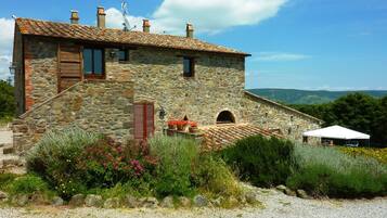 Una casa de piedra con techo de tejas, un pequeño jardín con flores y vistas al campo.