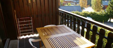 A wooden table and chairs on a balcony with a view of houses and trees.