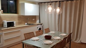 Ett modernt kök med mikrovågsugn, diskho och tvättmaskin. Det finns ett matbord dukat med tallrikar, glas och en röd skål.