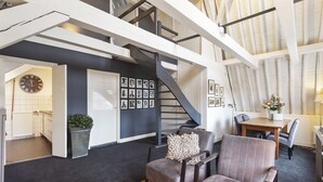 Un loft espacioso con techo alto, vigas de madera a la vista, una escalera y un área de estar con chimenea.