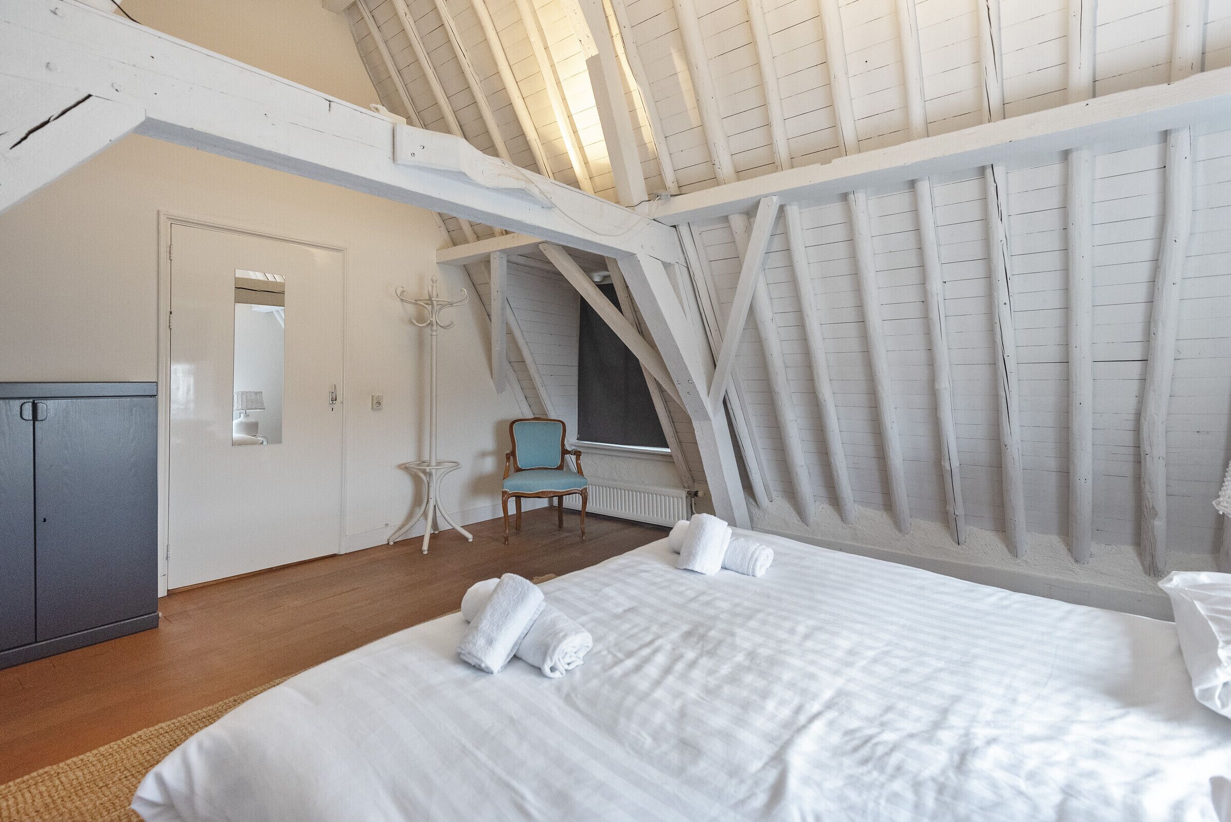 Een slaapkamer met een groot bed, een stoel, een kledingkast en een raam met uitzicht op de lucht.