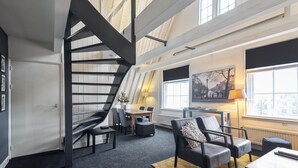 Un interior moderno con una escalera, zona de estar y ventanas amplias.