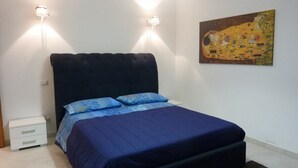 Une chambre à coucher avec un grand lit, deux lampes fixées au mur, une table de chevet et un tableau accroché au mur.