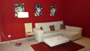 Un salon moderne avec un canapé blanc, un tapis rouge et trois œuvres d’art encadrées accrochées au mur.