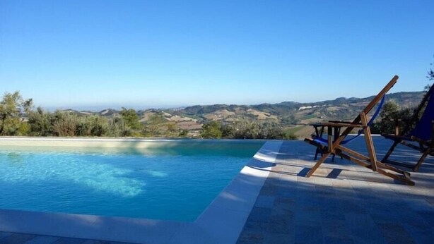Une piscine avec vue sur les collines, une chaise en bois et un fauteuil de jardin bleu.