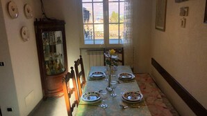 Une salle à manger avec une table dressée pour quatre personnes, un buffet en bois doté de portes en verre et une fenêtre donnant sur l’extérieur.
