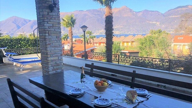 Un espace de restauration en plein air avec une table dressée pour quatre personnes, une bouteille de champagne et un saladier de fruits.