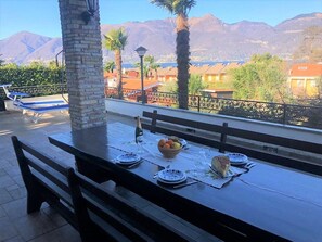 An outdoor dining area with a table set for four, a bottle of champagne, and a bowl of fruit.