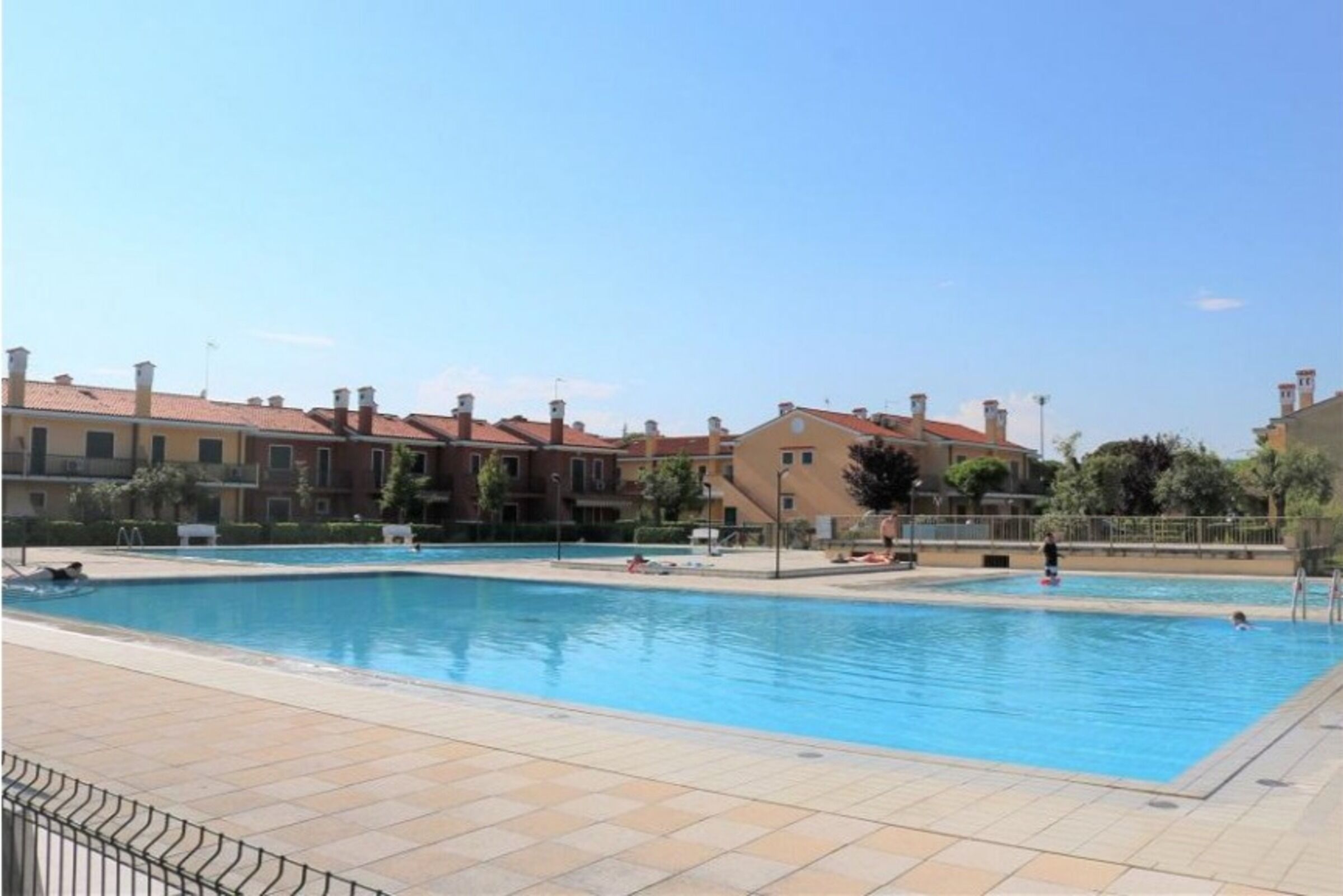 A swimming pool with tiled deck, surrounded by buildings with red-tiled roofs.