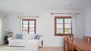 A room with a white sofa, a wooden dining table, and two windows with curtains.