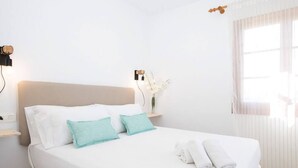A neatly made bed with white and teal pillows, a white duvet, and rolled towels on the side.
