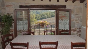 Un coin repas avec une table et des chaises, une plante en pot et une vue sur un paysage montagneux par de grandes portes vitrées.