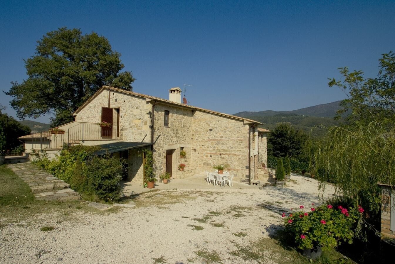 A stone house with a balcony, a gravel driveway, and a garden with potted plants.
