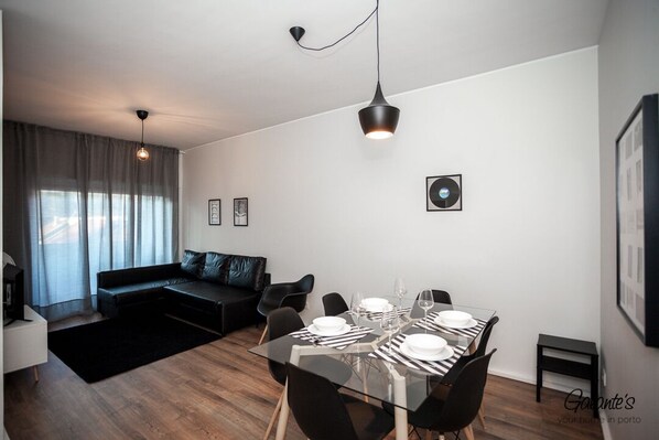 A modern living room with a glass dining table set for four, black chairs, a black sofa, and a black coffee table.
