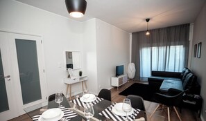 Un salon moderne comprenant un coin repas, un canapé, un téléviseur et une fenêtre avec des rideaux.