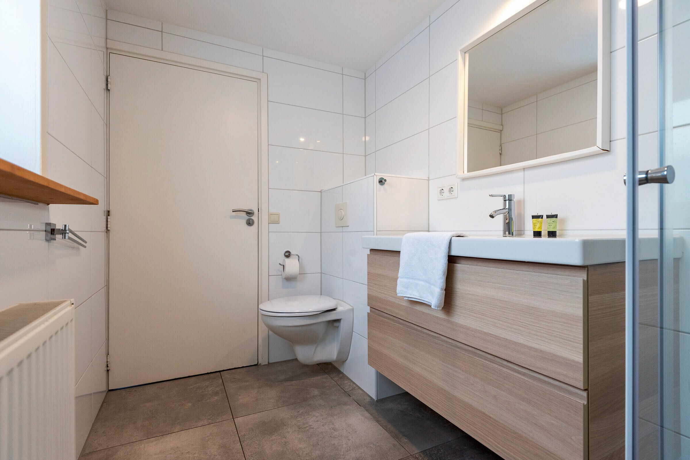 Un baño moderno con inodoro, lavabo con espejo y una toalla colgada en la pared.