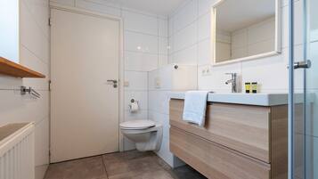 Un baño moderno con inodoro, lavabo con espejo y una toalla colgada en la pared.