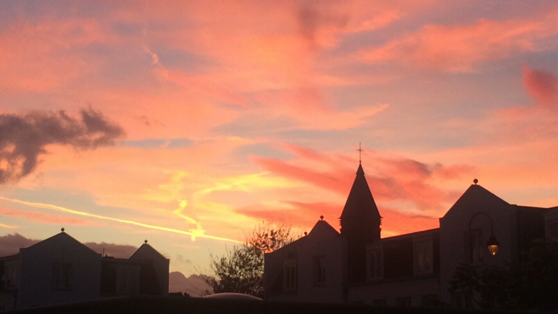 Une église dotée d’un clocher imposant et surmontée d’une croix, entourée d’immeubles d’habitation, le tout baigné par les couleurs du coucher de soleil.