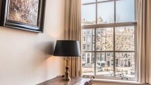 Ein Zimmer mit einem Holztisch, einer Lampe und einem Fenster mit Blick auf Gebäude.