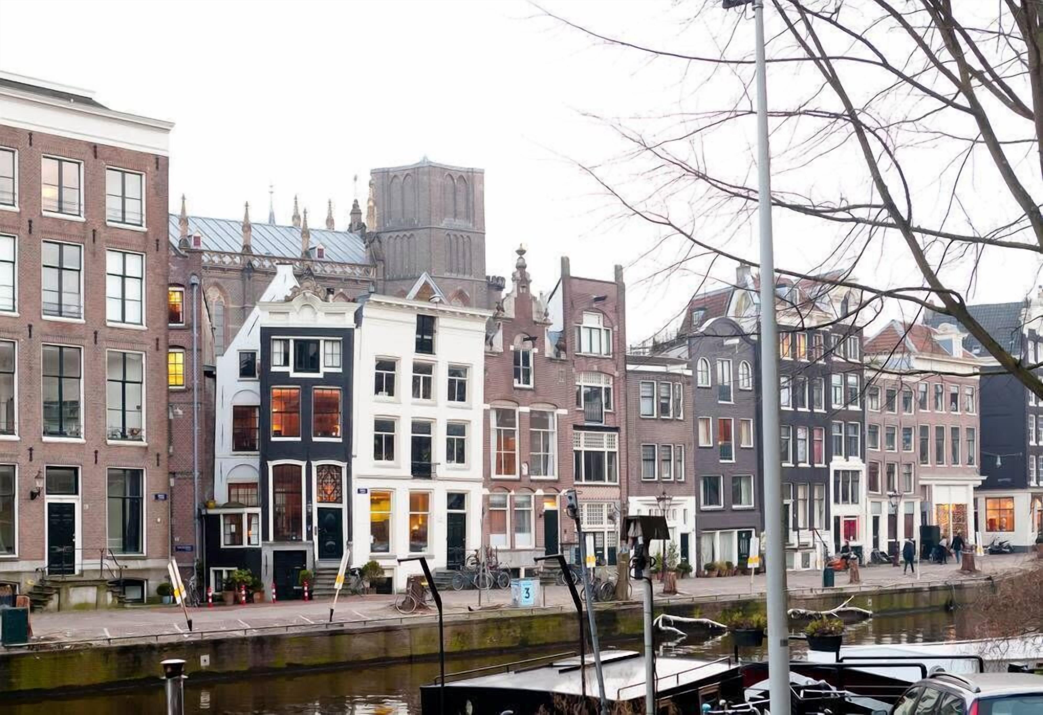 A canal-side street with historic buildings, a narrow pedestrian path, and a boat dock.