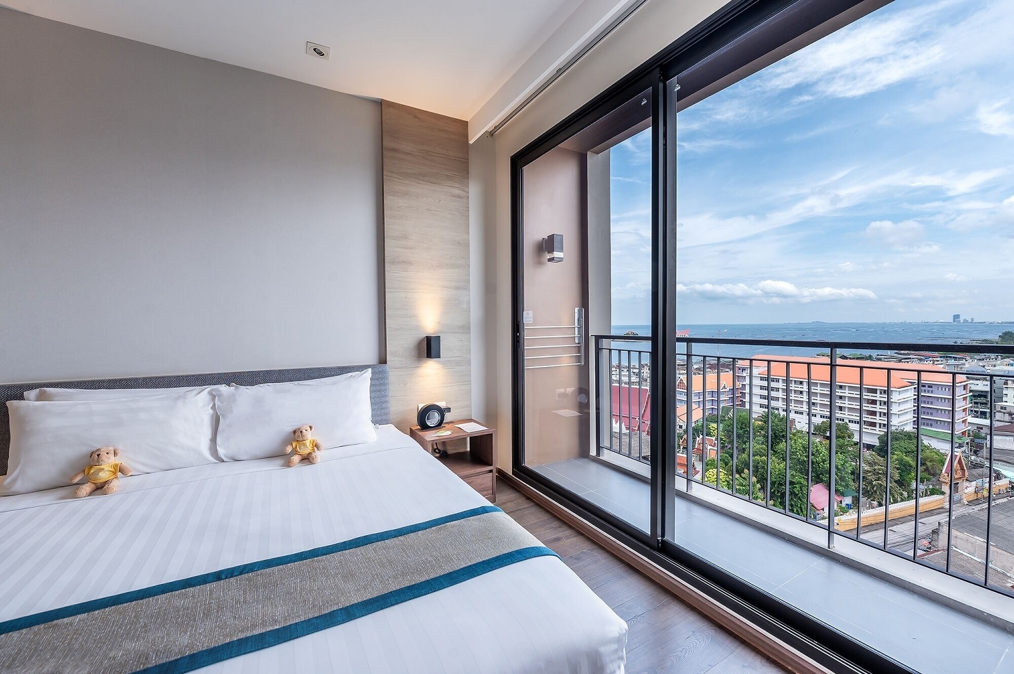Ein modernes Hotelzimmer mit einem großen Bett, einem Nachttisch, einem Teddybären und einem Balkon mit Blick auf die Stadt.