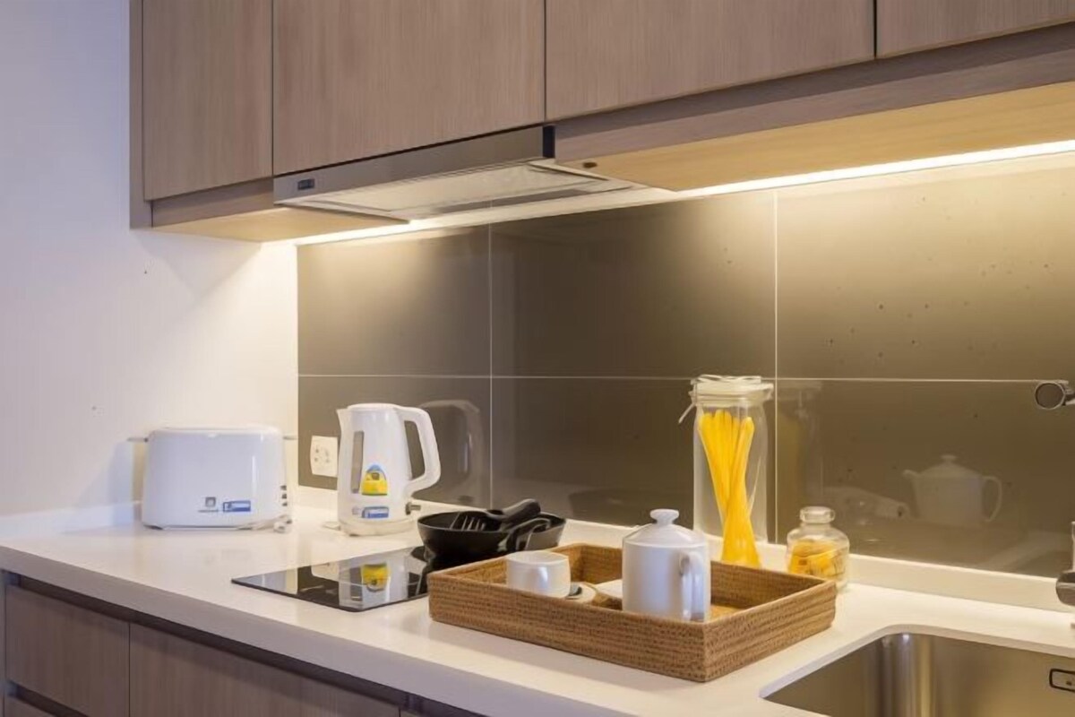 A modern kitchen with a white countertop, a coffee maker, a kettle, a frying pan, a basket with a mug, and a glass jar.
