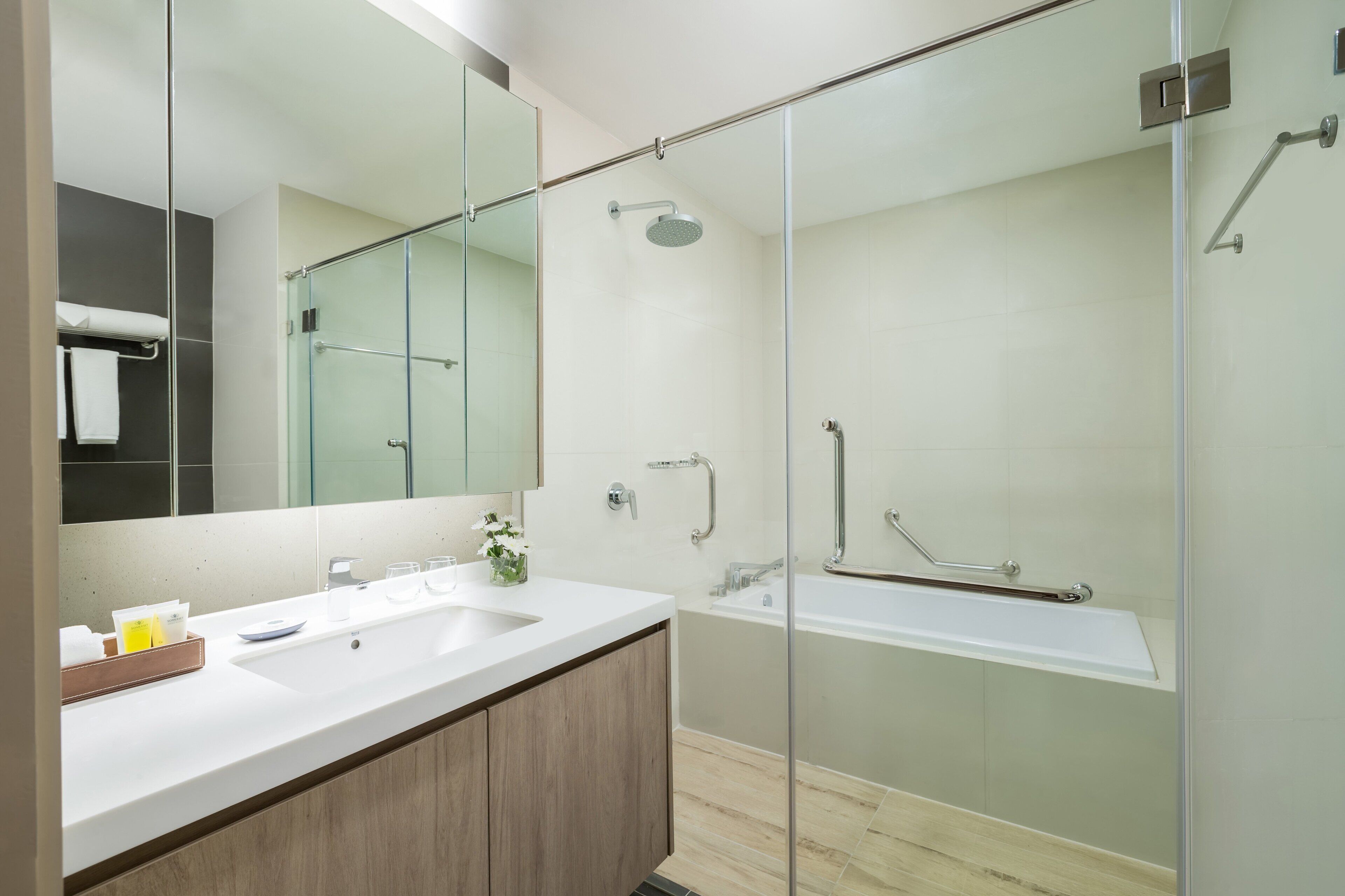 A modern bathroom with a glass-enclosed shower, a large mirror, and a wooden vanity.
