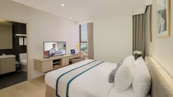 Habitación de hotel moderna con una cama grande, un escritorio con computadora, televisor y un baño visible a través de una puerta abierta.