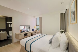Habitación de hotel moderna con una cama grande, un escritorio con computadora, televisor y un baño visible a través de una puerta abierta.