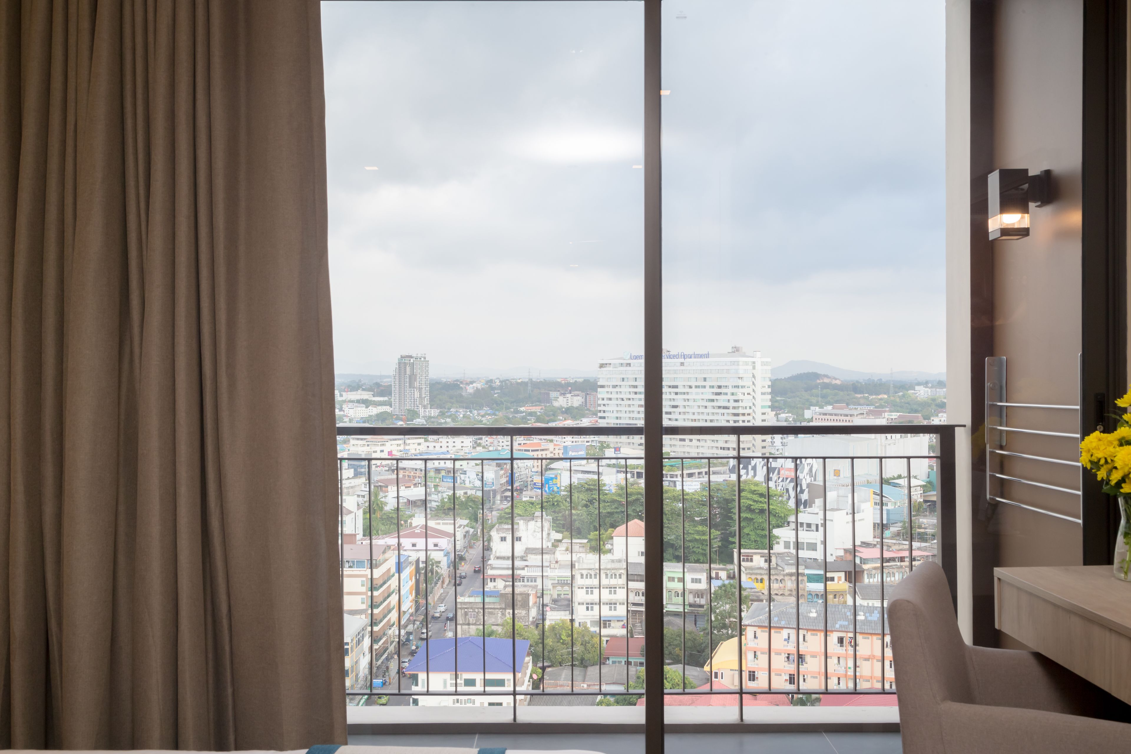 Ein Zimmer mit großem Fenster, Blick auf eine Stadtlandschaft und einem Balkon mit Geländer.