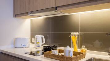 A modern kitchen with a built-in stove, a coffee maker, a kettle, and a basket with utensils.