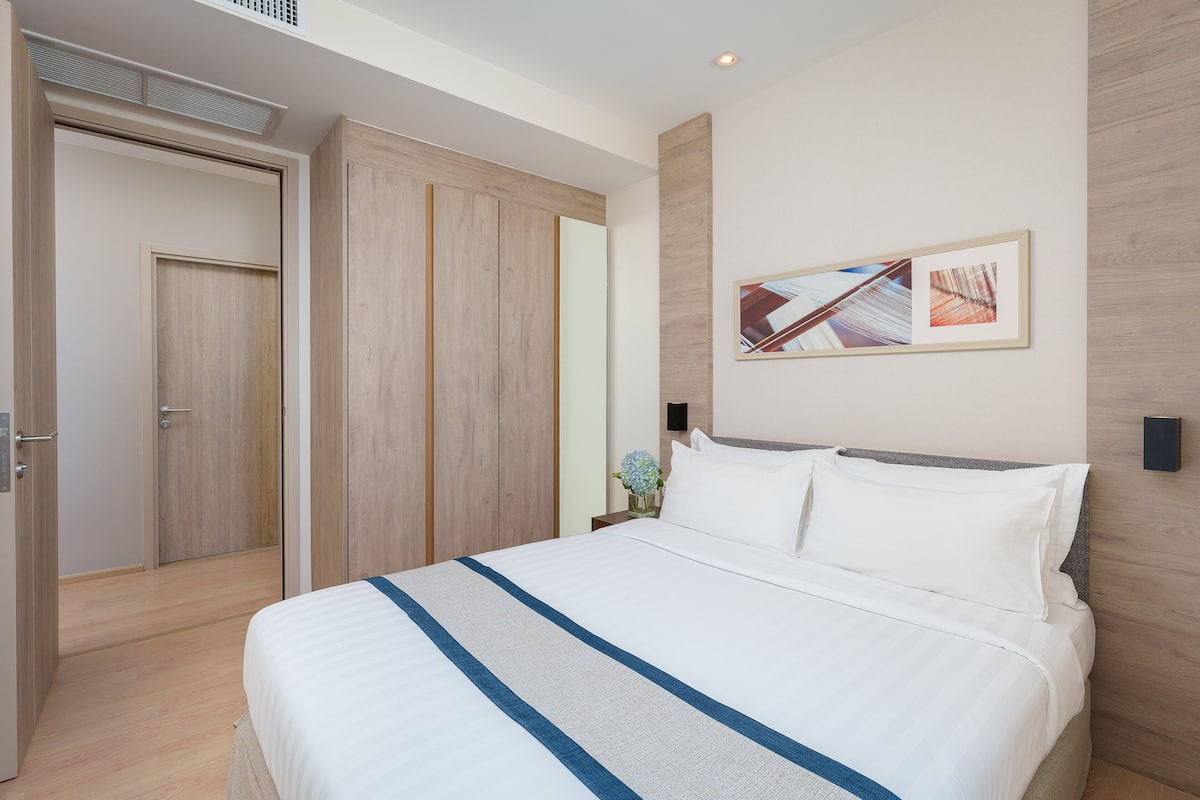 Ett modernt hotellrum med en stor säng, ett träskåp och ett inramat konstverk på väggen.