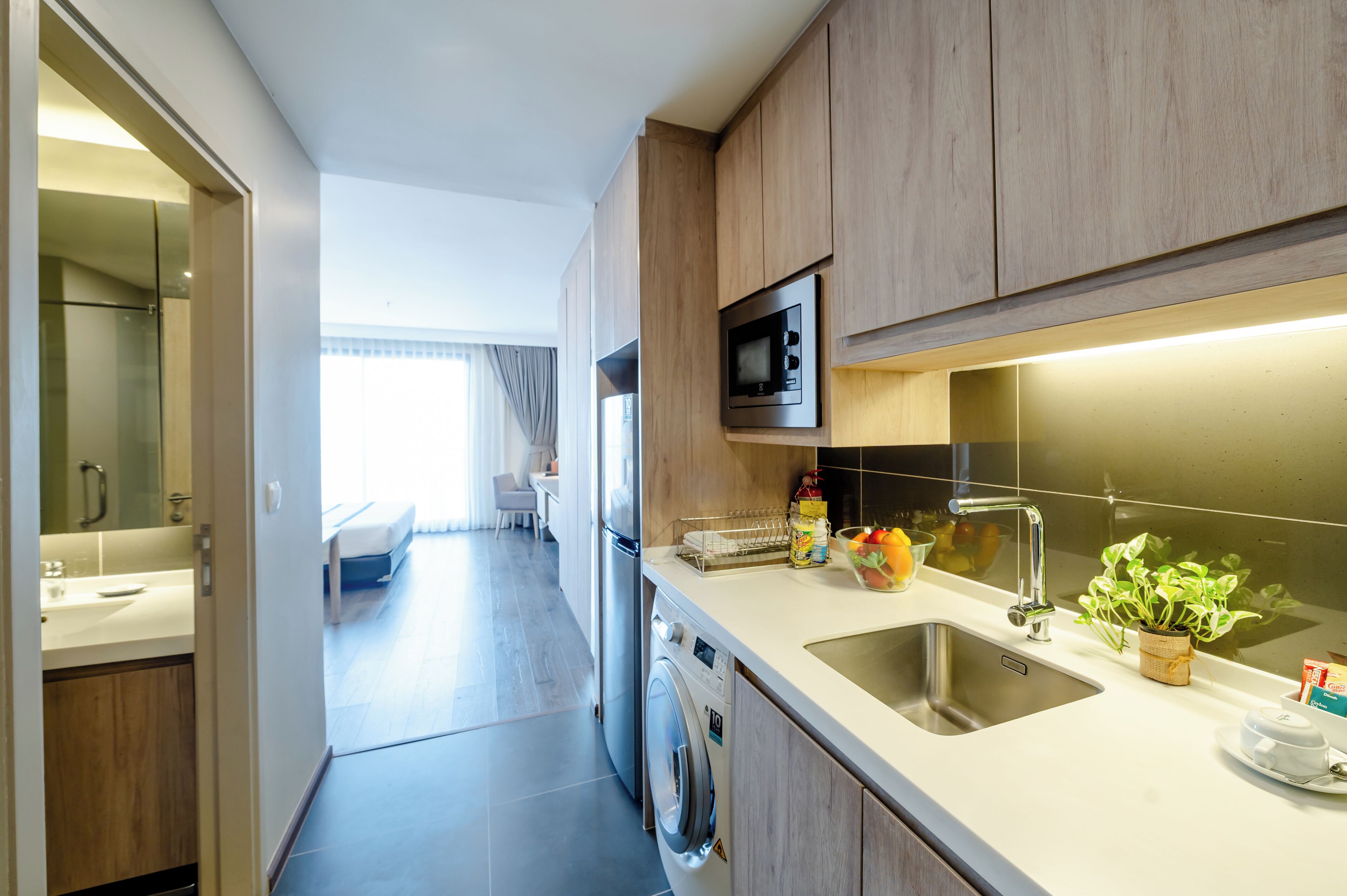 Una cocina moderna con armarios de madera, un microondas integrado, un lavamanos de acero inoxidable y una lavadora.