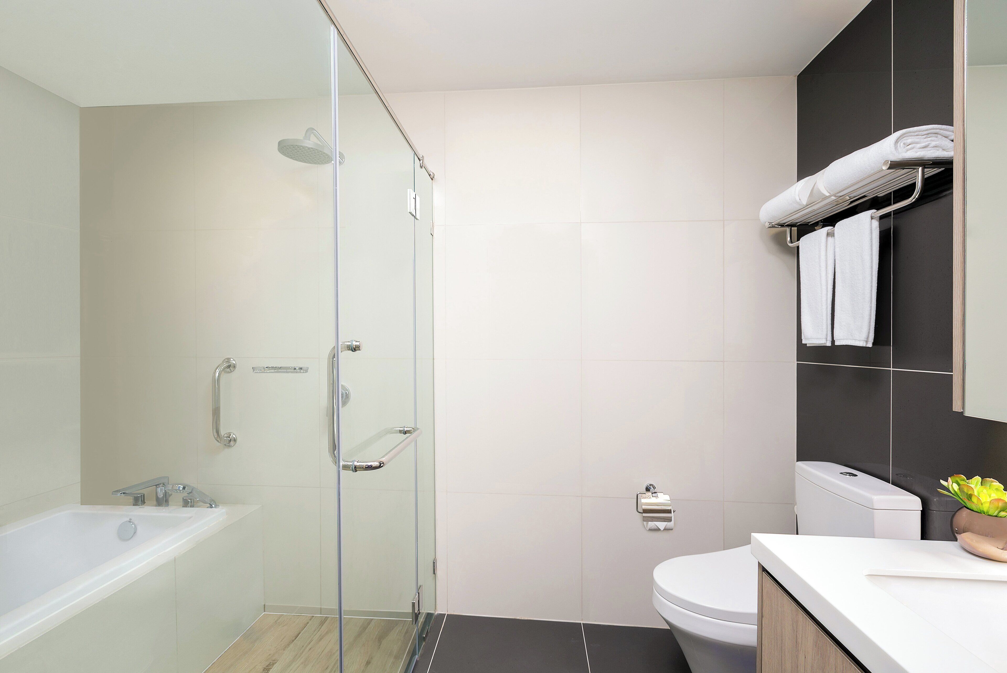 A modern bathroom with a glass-enclosed shower, a white bathtub, a toilet, and a sink with a countertop.