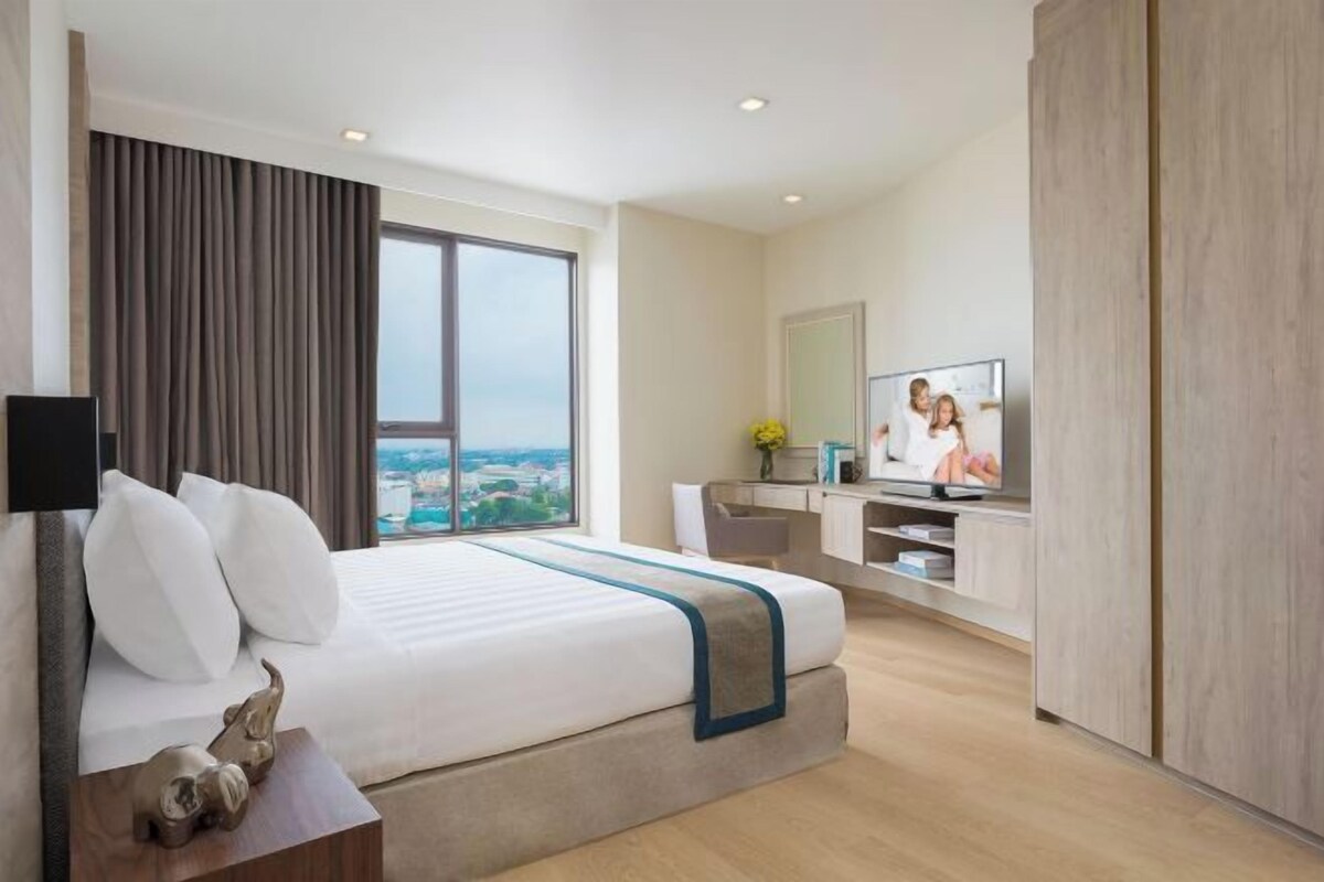 A hotel room with a large bed, a TV, a desk, and a view of the city.