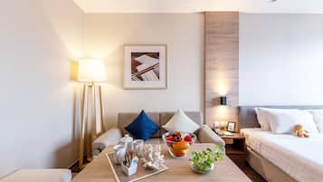 A modern hotel room with a sofa, a small table with a fruit bowl, a lamp, and a bed.