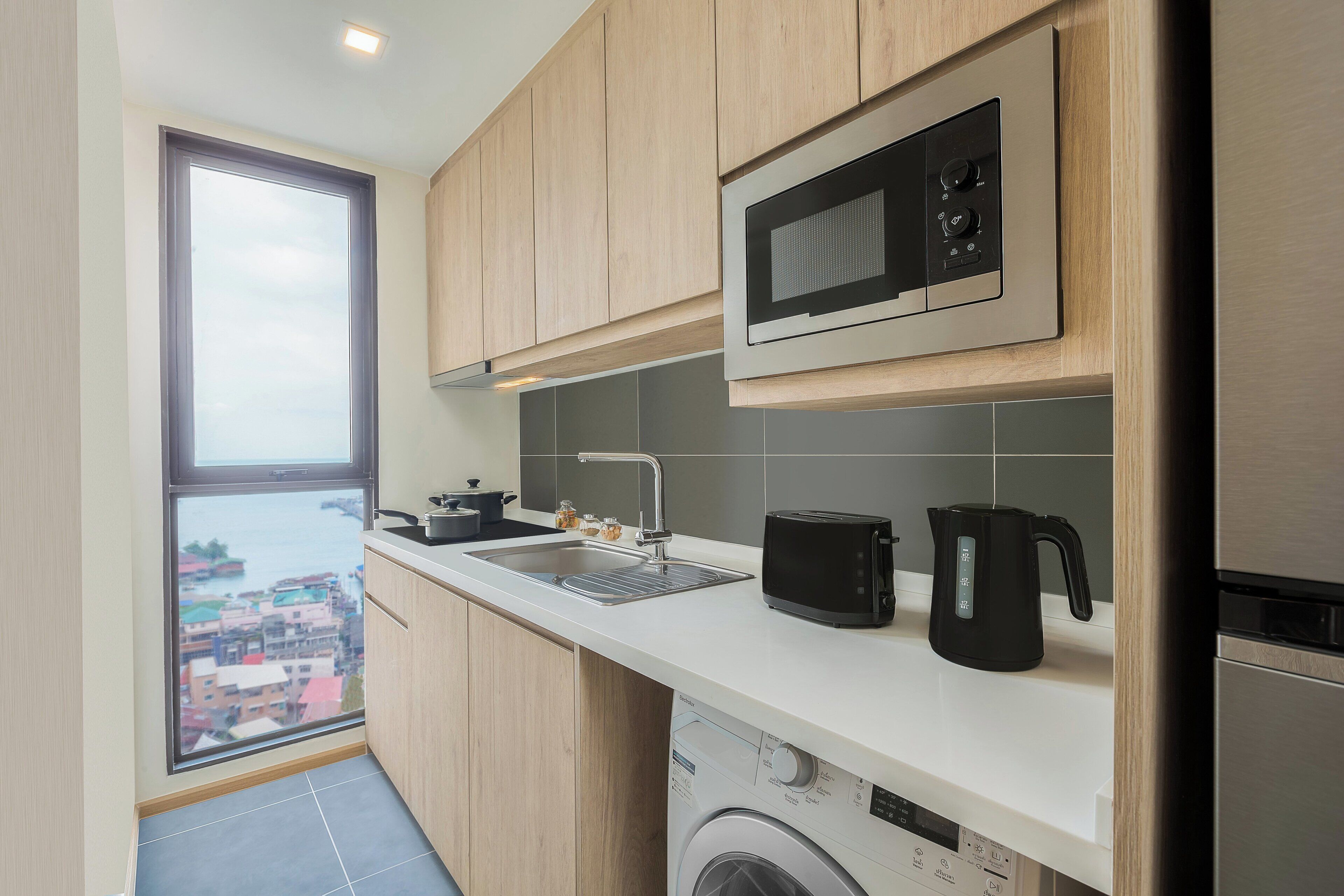 A modern kitchen with wooden cabinets, a built-in microwave, a toaster, and a washing machine.