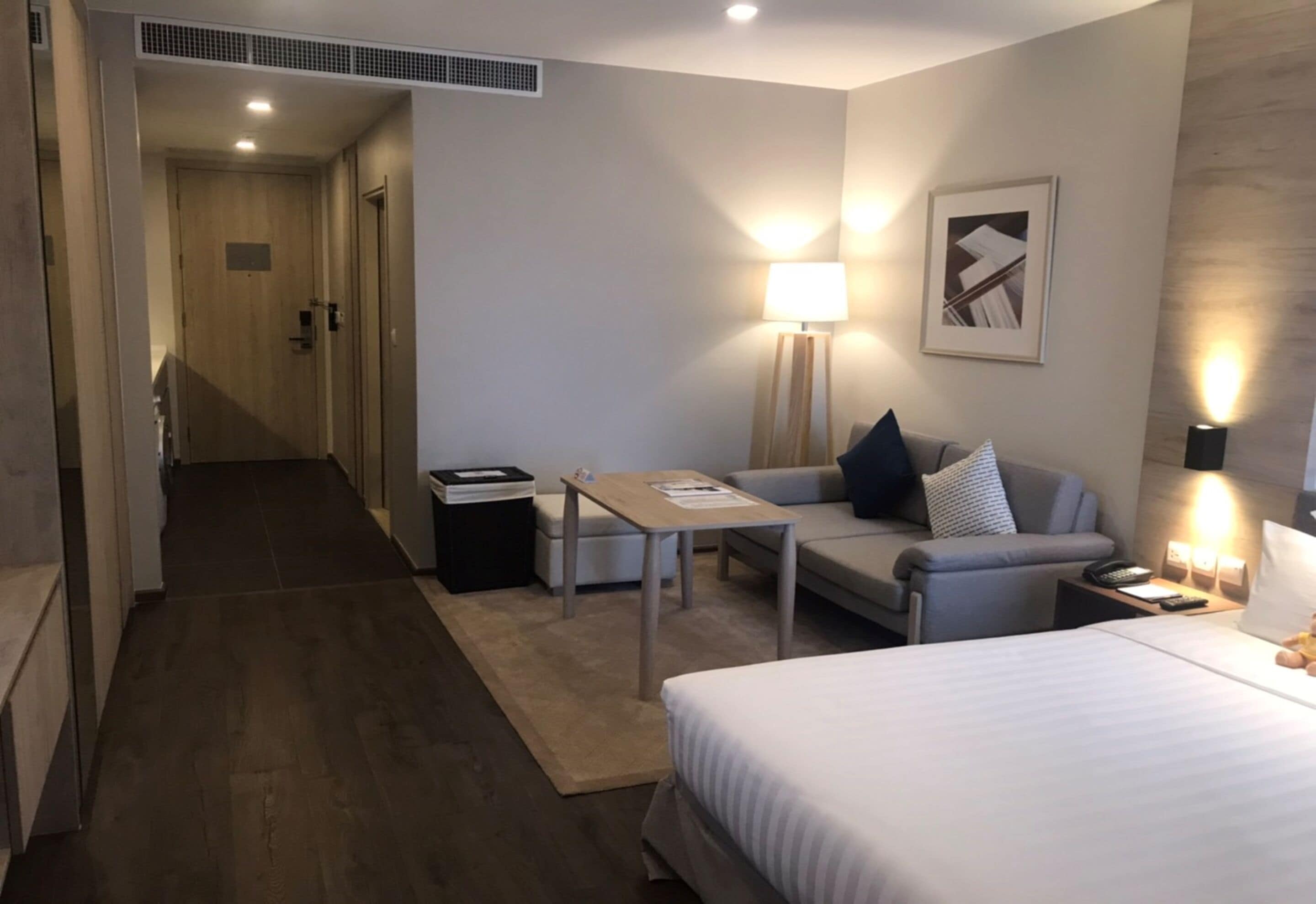 A hotel room with a bed, a sofa, a small table, a lamp, and a picture on the wall.