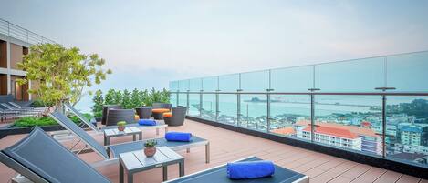 A rooftop terrace with lounge chairs, tables, and potted plants.