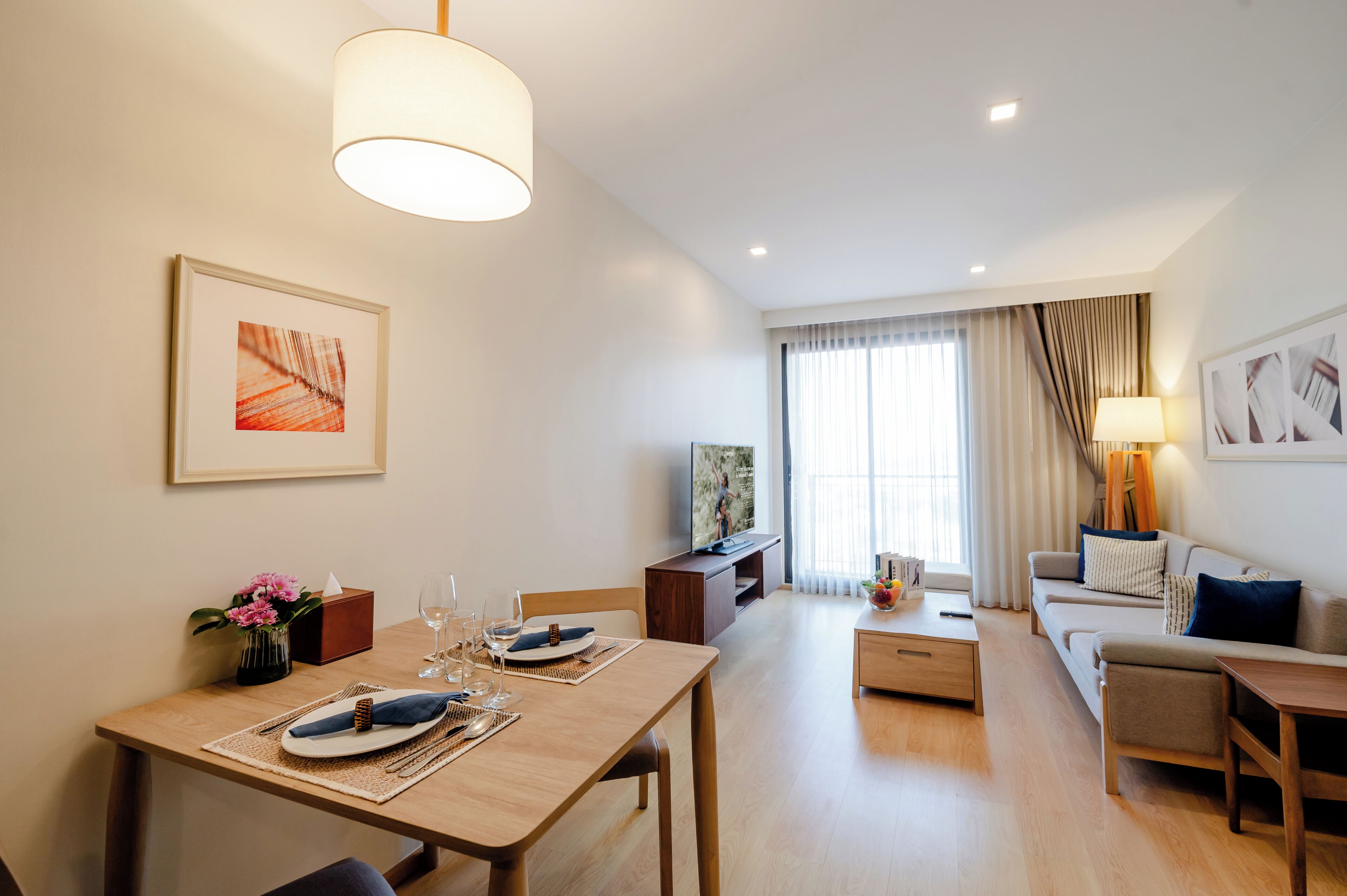 A modern living room with a dining area, a sofa set, a TV, and a large window with curtains.