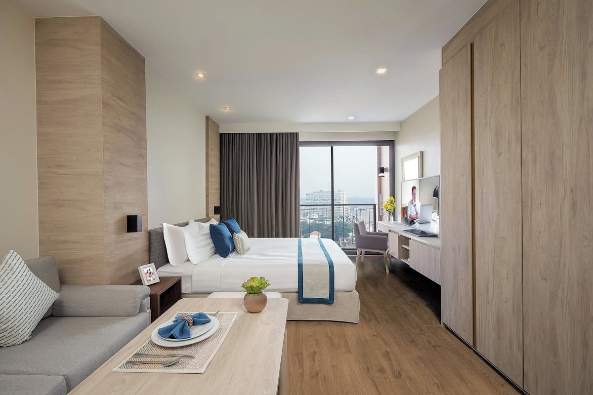 Ett modernt hotellrum med en stor säng, en soffa, ett skrivbord och utsikt över staden.