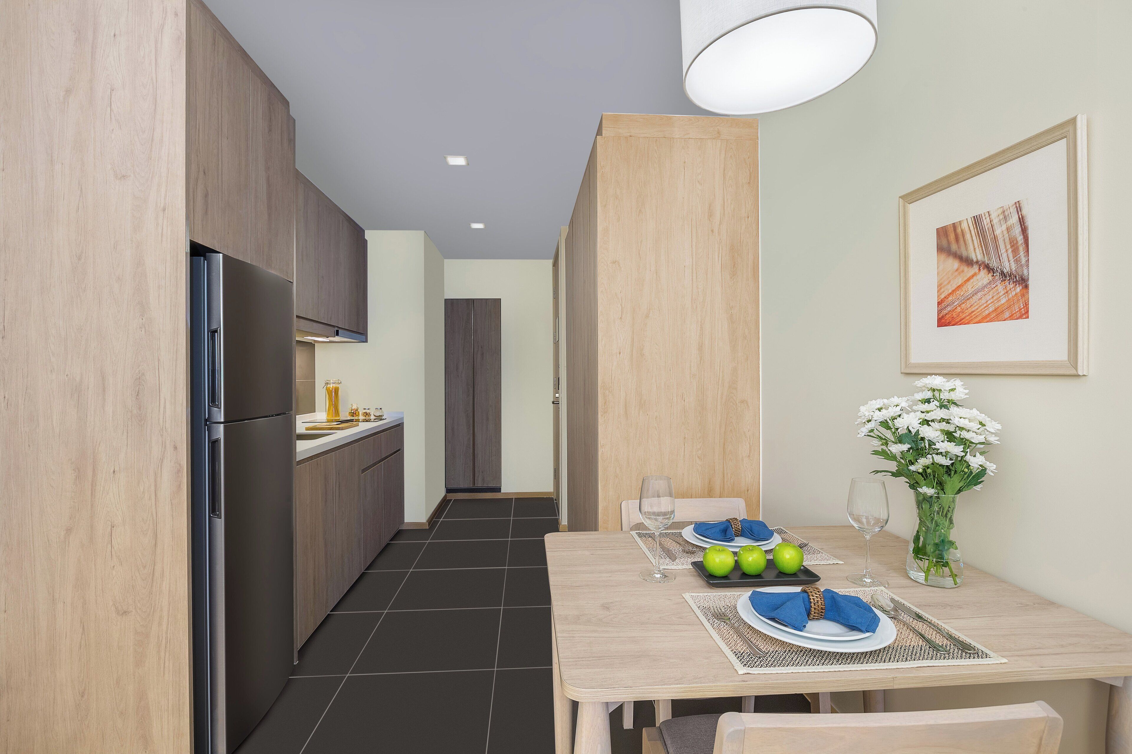 A modern kitchen with wooden cabinets, a stainless steel refrigerator, and a dining area with a table set for two.