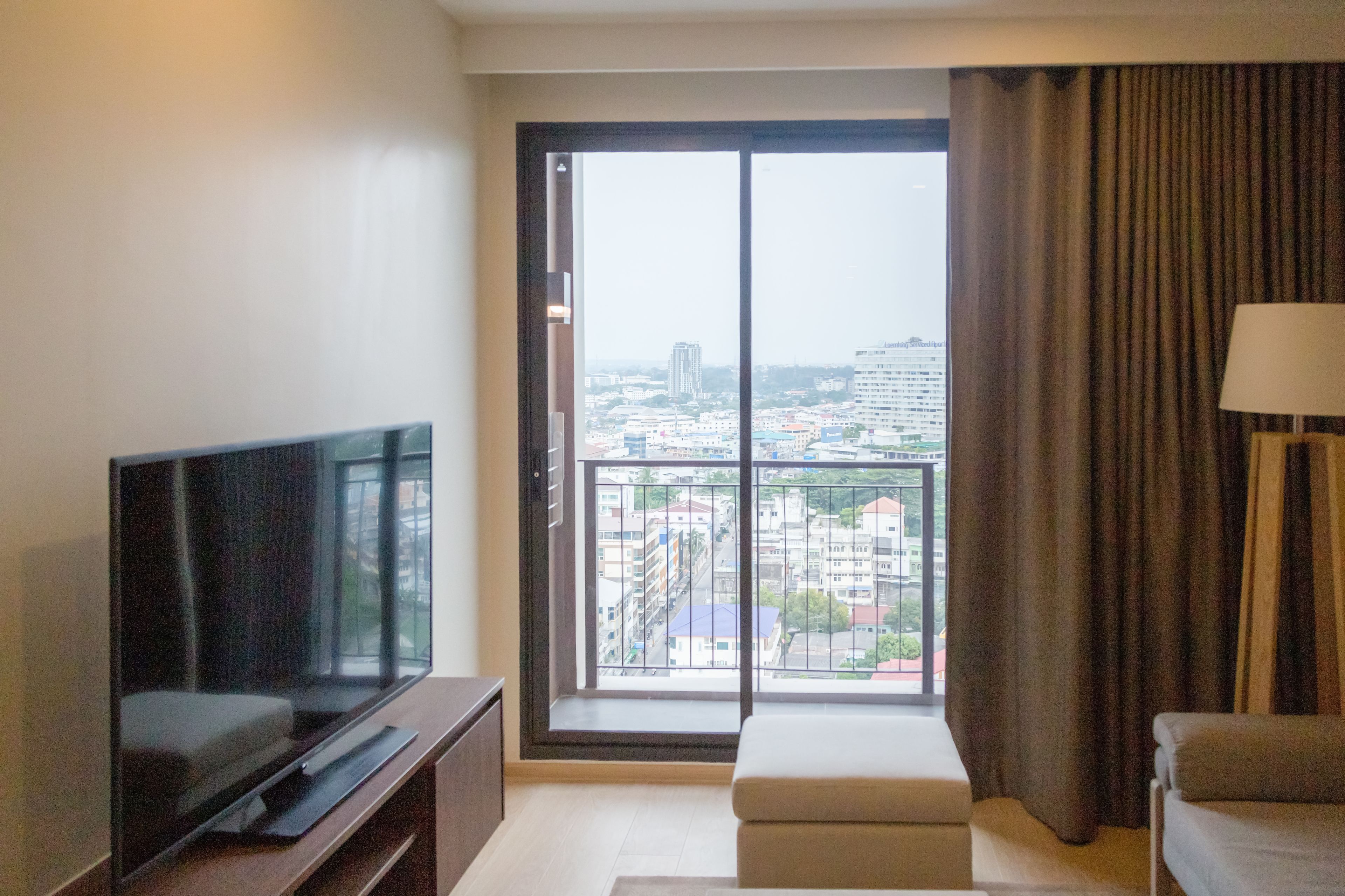Habitación de hotel con un ventanal grande, televisor de pantalla plana, sofá y lámpara.