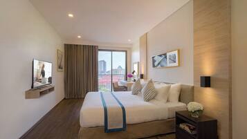 A modern hotel room with a large bed, a desk, a TV, and a view of the city through the window.