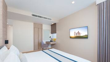 A hotel room with a bed, a desk with a chair, a mirror, a picture on the wall, and a window with curtains.