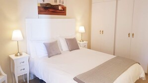 Een netjes ingerichte slaapkamer met een groot bed, twee nachtkastjes met lampen, een kledingkast en een schilderij aan de muur.